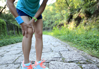 woman runner hold sports injured knee on forest trail. 