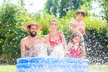 Familie spitzt mit Wasser im Garten Swimming Pool bei Abkühlung, Mutter, Vater und Kinder in einem...
