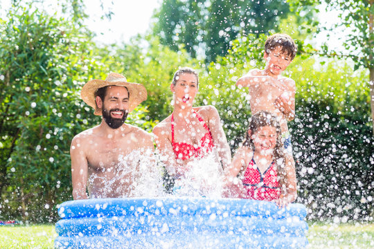 Familie spitzt mit Wasser im Garten Swimming Pool bei Abk&uuml;hlung, Mutter, Vater und Kinder in einem Becken