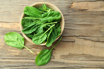Bowl of fresh spinach leaves on wooden background