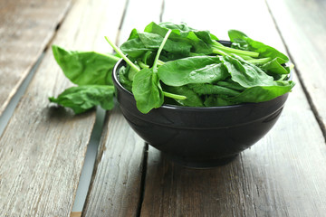 Bowl of fresh spinach leaves on wooden background