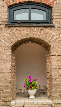 Blooming flowers in a vase in the portal brick-stone wall of a m