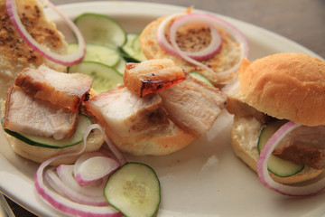 A platter of roast pork belly, cucumbers, onions and small rolls spread with whole grain mustard