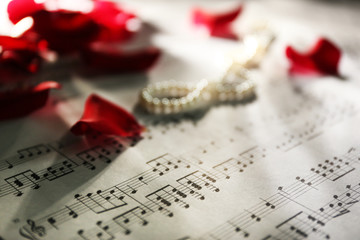 Beautiful rose petals with pearls on music sheets background