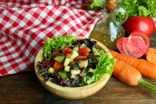 Wooden bowl of fresh vegetable salad on wooden table, closeup