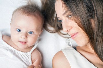 Happy mother with a baby lying on a white bed