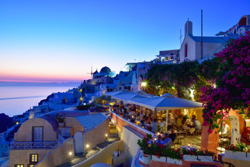 Dusk scene on the seaside with public terrace in evening lights in Oia Santorini, Greece