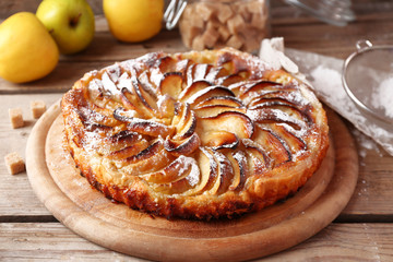 Homemade apple pie on cutting board and fresh apples on wooden background