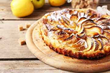 Homemade apple pie on cutting board and fresh apples on wooden background