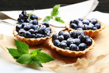 Delicious crispy tarts with black currants on parchment on wooden board, closeup