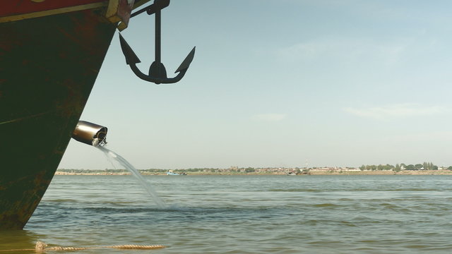 Close-up on the end of a dredge pipe section and an anchor hanging at the bow of a boat