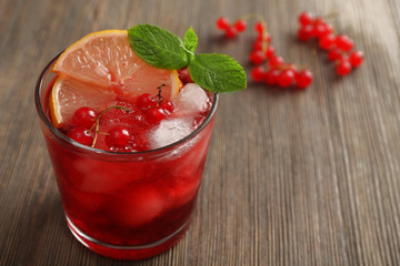 Glass of red currants juice with lemon and ice cubes on wooden table, closeup