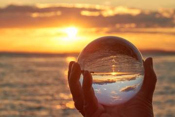 Die Sonne geht über dem Bodensee unter und leuchtet durch eine Glaskugel.