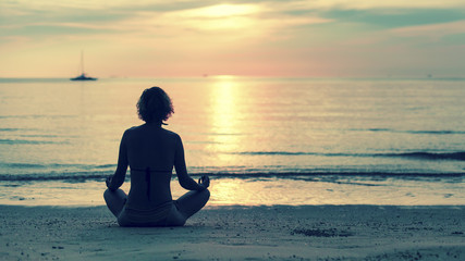 Yoga woman sitting in lotus pose on the beach during amazing sunset.