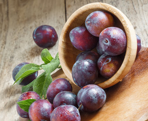 Blue plum poured from a wooden bowl, selective focus