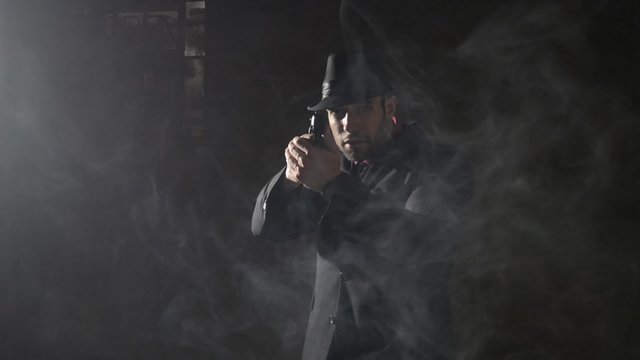 Man in a suit and hat drawing gun on a foggy night
