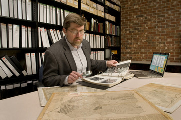 Researcher in archive, searching through maps and photographs
