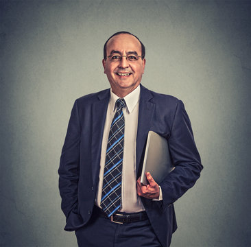 Happy businessman with glasses and laptop standing on gray background