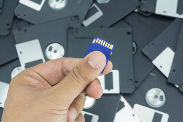 Hand holding SD card with floppy disk background