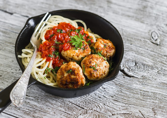 spaghetti with tomato sauce and chicken meatballs in a pan on a light wooden