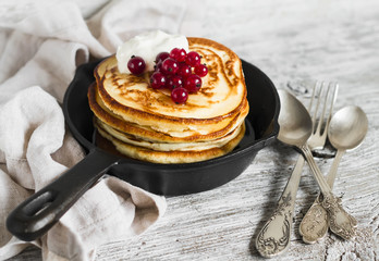 pancakes with honey and red currants in a pan on a light wooden background