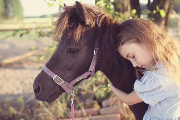 Young girl hugs a pony on a farm
