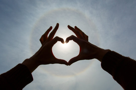 Lovers holding hands in shape of heart over a sunbow