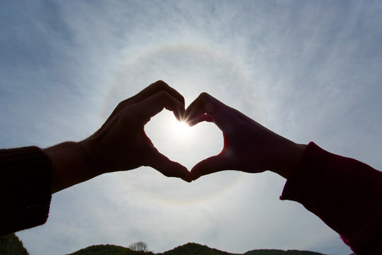 Lovers holding hands in shape of heart over a sunbow