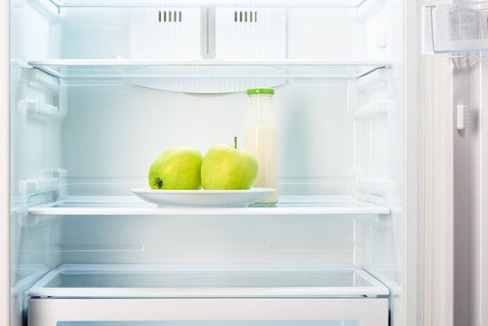 Two apples on plate and bottle of yoghurt in refrigerator
