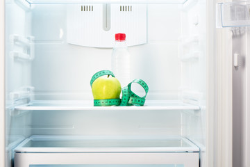 Apple with measuring tape and bottle on shelf of refrigerator