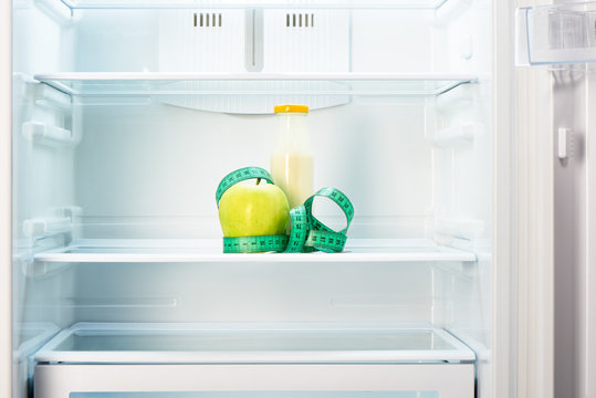 Apple with measuring tape and bottle on shelf of refrigerator