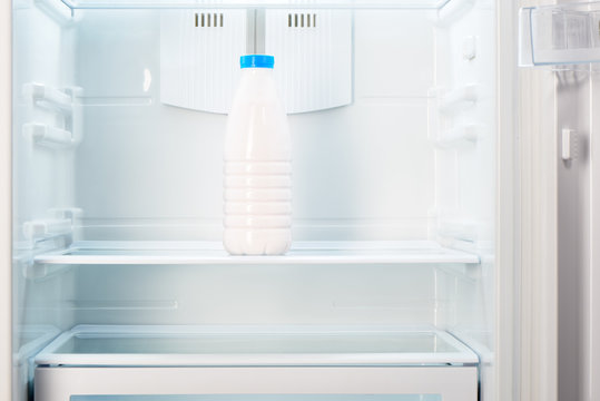 Bottle of yoghurt on shelf of open empty refrigerator