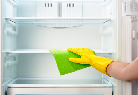 Woman's hand in yellow glove cleaning refrigerator with green rag