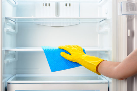 Woman's hand in yellow glove cleaning refrigerator with blue rag