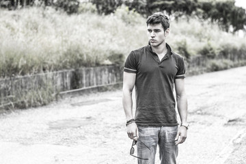 Young man in jeans and black t-shirt walking along rural road