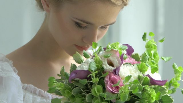 Blond girl in white dress with charming bouquet of flowers