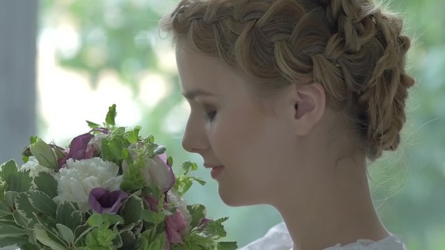 Young blonde girl in white vintage dress enjoys smeling flowers
