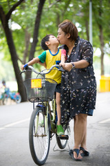 Asian Son on bicycle is kissing his mother in the park