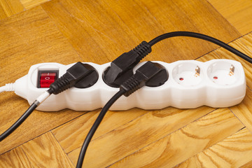 Many plugs plugged into electric power bar on floor