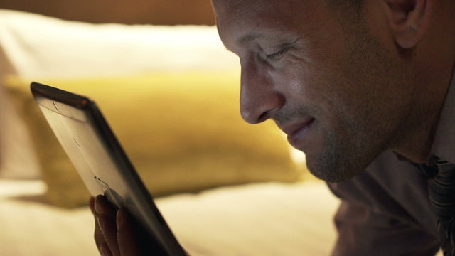 Young Businessman Watching Movie On Tablet Computer Lying On Bed At Night 
