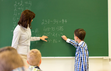schoolboy with math teacher writing on chalk board