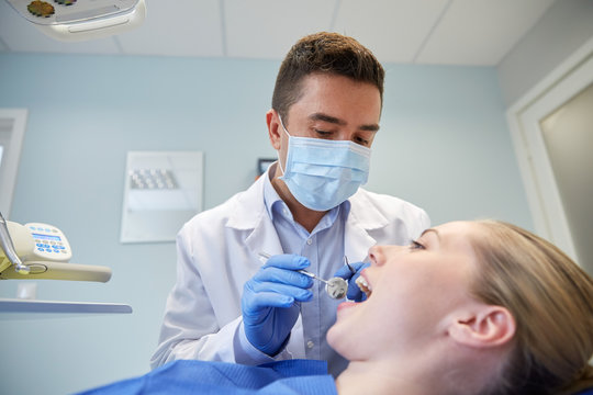 male dentist in mask checking female patient teeth