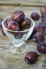 Obraz premium Vase of purple plums on wooden background, purple food