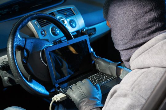 Car Thief Stealing A Car.  Starting The Car With A Lap Top Code Breaker.