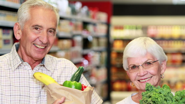 Senior couple with bag of veg in grocery store