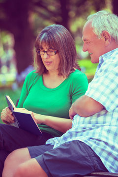 Happy senior couple in park reading Bible
