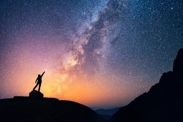 Catch the star. A person is standing next to the Milky Way galaxy pointing on a bright star. - obrazy, fototapety, plakaty