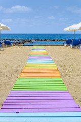 Colorful wooden walkway across the sand at the beach with lounge chairs and umbrellas leading to the sea