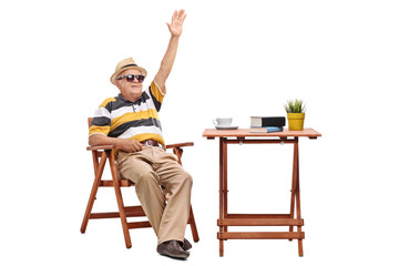 Senior man sitting at a table and waving with hand