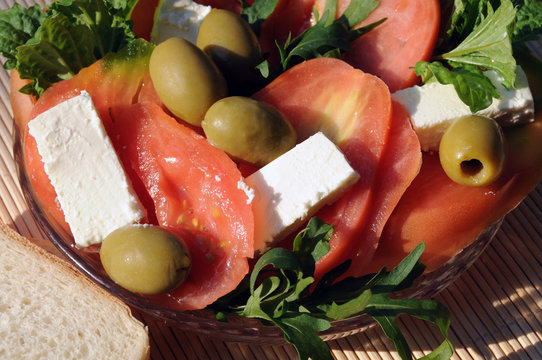 Light summer snack with tomatoes, feta cheese, rocket (eruca sativa), olives, lettuce leaf basil and toast